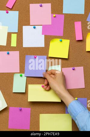 Une main tient un autocollant vierge pour écrire des idées sur un tableau de liège. Banque D'Images