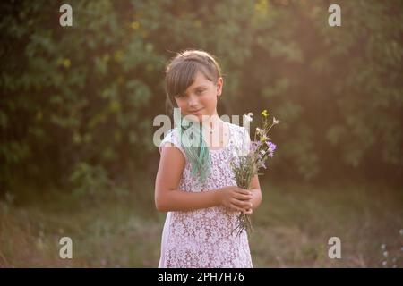 Fille à cheveux verts tient le bouquet de fleurs sauvages sur fond botanique, regarde dans l'appareil photo. Cadeau naturel doux pour la mère. Génération Z dans bri Banque D'Images