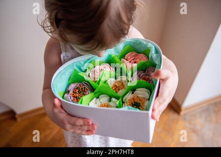 Vue du dessus gros plan portrait petite fille en forme de coeur tient boîte avec des guimauves maison, doux dans les mains. Produits écologiques faits maison sans Banque D'Images