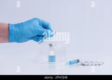 Sur fond blanc isolé se trouve le vaccin avec seringue, pilules. Le gant médical bleu ouvre le dôme de protection programmé. Contre-traiter Banque D'Images