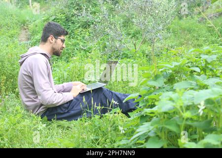 Homme travaillant à l'extérieur avec un ordinateur portable assis dans la nature. Concept de travail à distance ou de style de vie de freelance. Couverture large bande du réseau cellulaire. internet 5G. Banque D'Images