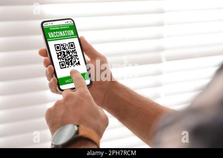 Homme portant un smartphone avec certificat international de vaccination à l'intérieur, gros plan Banque D'Images