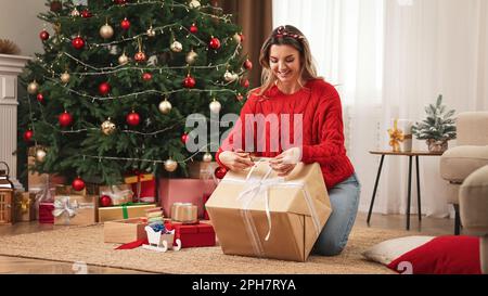 Belle jeune femme emballage cadeau près de l'arbre de Noël à la maison Banque D'Images