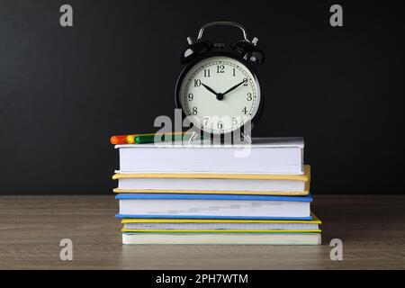 Réveil et livres empilés sur une table en bois près du tableau noir. Temps d'école Banque D'Images