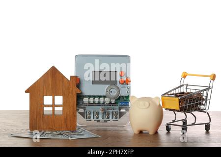 Compteur d'électricité, modèle de maison, banque de porc et chariot avec de l'argent sur table en bois sur fond blanc Banque D'Images