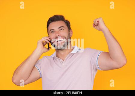 Homme excité dans un t-shirt utilisant un téléphone portable isolé sur fond de studio. Portrait de confiance d'un homme hispanique millénaire d'âge moyen utilisant un téléphone portable Banque D'Images