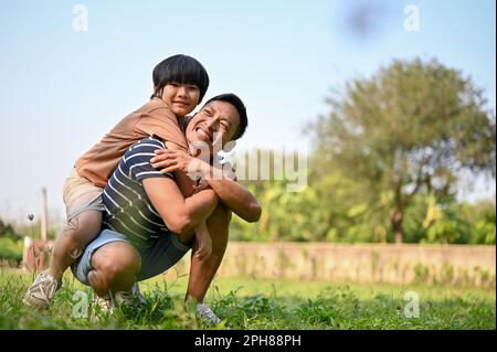 Souriant et heureux papa asiatique jouant avec son fils dans l'arrière-cour tout en le portant sur son dos. posture du porcgyback. concept de famille heureuse et de papa unique Banque D'Images