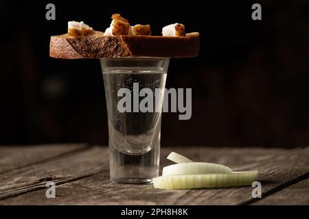 Un verre de vodka à côté d'un morceau de pain noir avec du bacon sur une table en bois dans la cuisine pour le déjeuner en ukrainien Banque D'Images