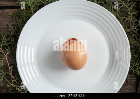 un œuf de poulet cassé repose sur une plaque blanche sur la table Banque D'Images