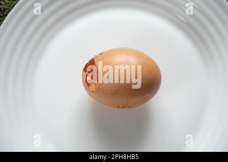 un œuf de poulet cassé repose sur une plaque blanche sur la table Banque D'Images