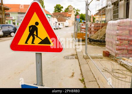 Signalisation rouge triangle pour les travaux routiers et signalisation bleue pour indiquer que la route aveugle est installée sur la chaussée devant le chantier de construction clôturé. Banque D'Images