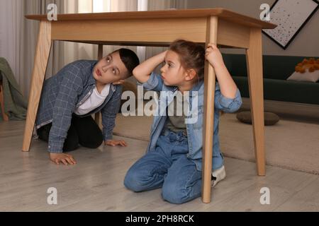 Des enfants effrayés se cachent sous la table dans le salon pendant le tremblement de terre Banque D'Images