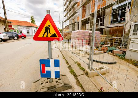 Signalisation rouge triangle pour les travaux routiers et signalisation bleue pour indiquer que la route aveugle est installée sur la chaussée devant le chantier de construction clôturé. Banque D'Images