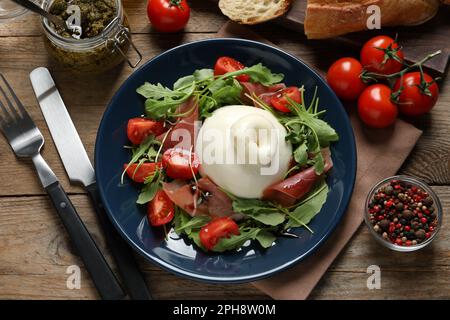 Salade burrata délicieuse avec tomates, prosciutto et arugula servi sur une table en bois, plat Banque D'Images