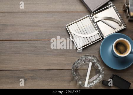 Étui avec cigarettes à filtre à tabac, cendrier en verre et tasse de café sur table en bois, plat. Espace pour le texte Banque D'Images