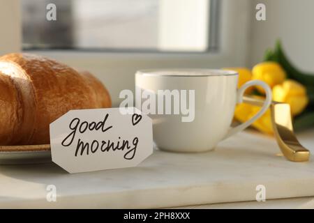 Tasse de café, croissant et carte avec phrase BONJOUR près de la fenêtre Banque D'Images