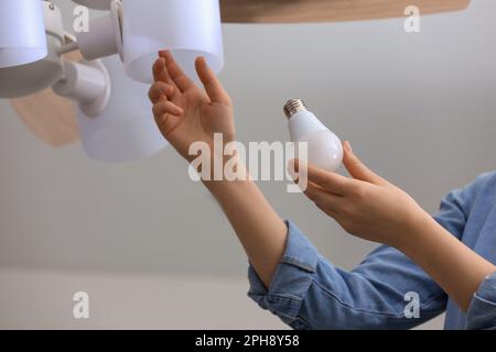 Femme changeant d'ampoule fluorescente dans la lampe de plafond à la maison, gros plan. Concept d'économie d'énergie Banque D'Images