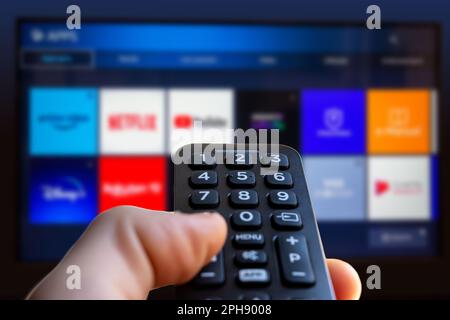 Un homme tient une télécommande de Smart TV avec un écran de télévision en arrière-plan avec une icône d'application de service de streaming vidéo Banque D'Images