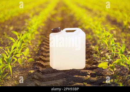 Canister blanc vierge d'herbicide dans le champ de semis de maïs au coucher du soleil de printemps, foyer sélectif Banque D'Images