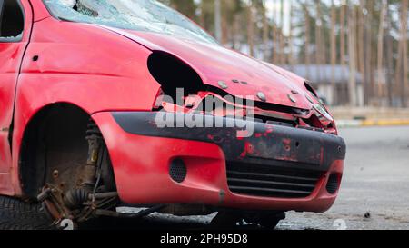 Une petite voiture rouge cassée et grondée se tient sur le côté de la route sans phares et une roue après un coup puissant. Accident dans la rue, endommagé c Banque D'Images