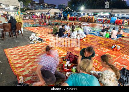 Phnom Penh,Cambodge-23 décembre 2022:comme le crépuscule tombe, les voyageurs Khmers et occidentaux s'assoient en petits groupes sur des tapis, dans une grande zone, entouré par des stands de nourriture Banque D'Images