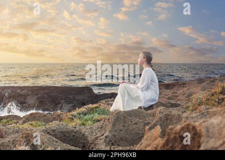 Adolescente assise sur des rochers près de la mer bleue Banque D'Images