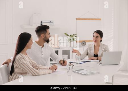 Un jeune couple heureux signant un contrat d'achat dans le bureau de l'agent immobilier. Concept hypothécaire Banque D'Images