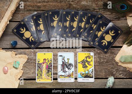 Cartes de tarot, plumes de paon, pierres précieuses et vieux livre sur table en bois, plat Banque D'Images