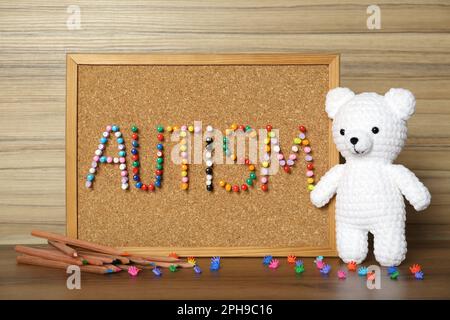 Tableau en liège avec le mot autisme fait de broches colorées, crayons et jouets sur table en bois Banque D'Images