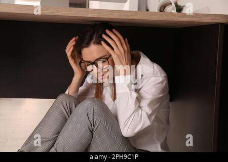 Une jeune femme effrayée se cachant sous le bureau pendant le tremblement de terre Banque D'Images