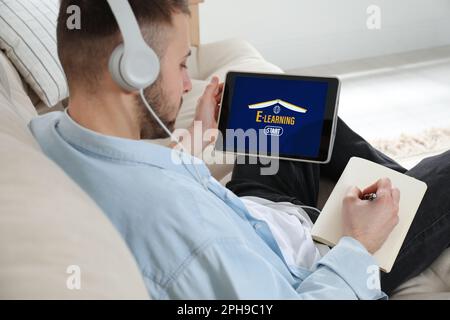 Jeune homme avec casque utilisant une tablette moderne pour étudier à la maison, gros plan. E-learning Banque D'Images