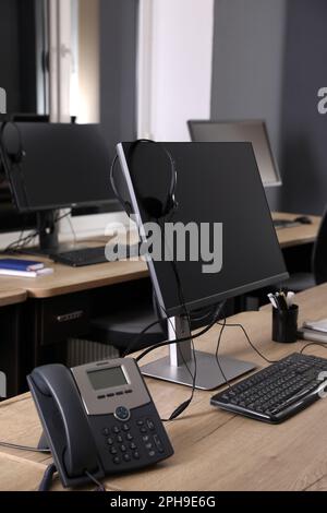 Ordinateur moderne avec casque et téléphone fixe sur bureau en bois. Service d'assistance téléphonique Banque D'Images