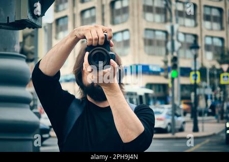 Portrait d'un jeune photographe caucasien adulte prenant une photo avec un appareil photo contre une ville floue à l'arrière-plan Banque D'Images