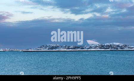 Morgenstimmung auf der Insel Senja und Kvaløya im Winter in Norwegen. DAS Morgenrot färbt schneebematte Berge und Wolken rötlich, lits Haus am Ufer Banque D'Images