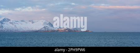 Morgenstimmung auf der Insel Senja und Kvaløya im Winter in Norwegen. DAS Morgenrot färbt schneebematte Berge und Wolken rötlich, lits Haus am Ufer Banque D'Images
