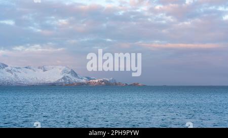 Morgenstimmung auf der Insel Senja und Kvaløya im Winter in Norwegen. DAS Morgenrot färbt schneebematte Berge und Wolken rötlich, lits Haus am Ufer Banque D'Images