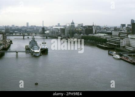 Londres. 1984. Vue vers l'ouest depuis le pied supérieur de Tower Bridge, enjambant la Tamise à Londres (Angleterre). Amarré sur la rivière est le croiseur de bataille de la Royal Navy de la seconde Guerre mondiale, H.M.S. Belfast, avec un autre navire à côté. Au-delà se trouve London Bridge et le pont ferroviaire de Cannon Street. Sur la rive nord, le Northern & Shell Building, situé au 10 Lower Thames Street, est en construction. La Tour de la poste, la Cathédrale Saint-Paul et le Monument sont visibles sur la ligne d’horizon. Banque D'Images