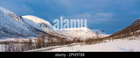 Morgenstimmung auf der Insel Senja und Kvaløya im Winter in Norwegen. DAS Morgenrot färbt schneebematte Berge und Wolken rötlich, lits Haus am Ufer Banque D'Images