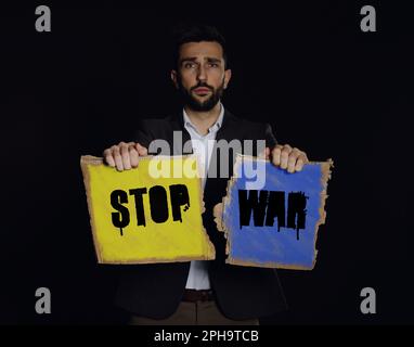 Homme malheureux tenant signe avec l'expression Stop War sur fond noir Banque D'Images