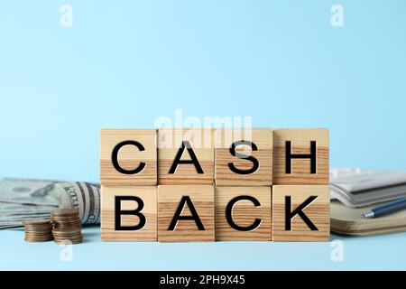 Mot Cashback fait avec des cubes en bois, des pièces de monnaie et des billets sur fond bleu clair Banque D'Images