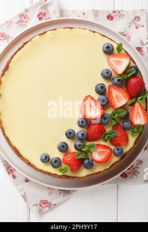 Gâteau au fromage classique de style New-yorkais avec baies fraîches et fermeture à la menthe sur l'assiette de la table en bois. Vue verticale du dessus Banque D'Images