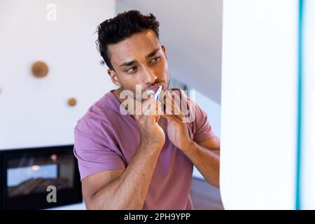 Homme biracial se regardant dans le miroir et se brossant les dents dans la salle de bains Banque D'Images