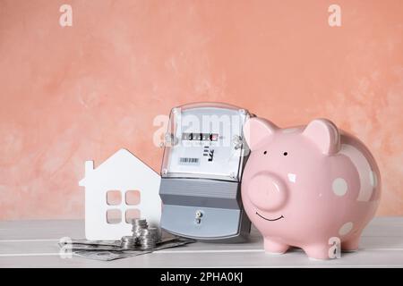 Compteur d'électricité, banque de porc, modèle de maison et argent sur table en bois blanc Banque D'Images