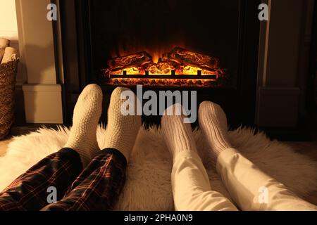 Couple en chaussettes tricotées près de la cheminée à la maison, gros plan des jambes Banque D'Images