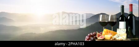 Vin savoureux, raisins et fromages sur table en bois contre beau paysage de montagne, espace pour le texte. Bannière Banque D'Images