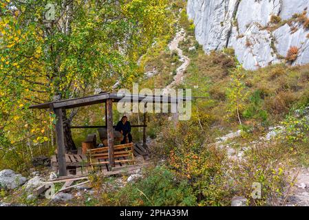 Une femme de tourisme âgée s'assoit seule dans un belvédère en bois sous une montagne dans l'Altaï en Sibérie. Banque D'Images