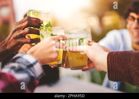 Un groupe d'amis multiraciaux se réunit dans un bar en plein air et toast avec des lunettes Mojito - gros plan sur les lunettes, avec le visage des amis Banque D'Images
