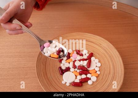 De dessus de la récolte anonyme main femelle avec cuillère sur plaque ronde avec divers médicaments et médicaments colorés Banque D'Images