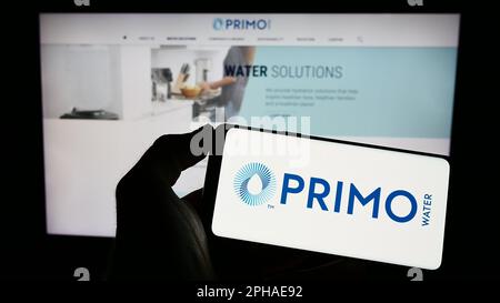 Personne tenant le téléphone portable avec le logo de la société américaine Primo Water Corporation sur l'écran en face de la page Web d'affaires. Mise au point sur l'affichage du téléphone. Banque D'Images