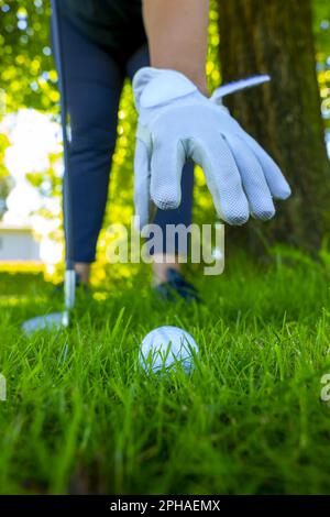 Balle de golf couchée sur l'herbe rugueuse et golfeur avec gant de golf ramasser la balle de golf dans l'herbe en une journée ensoleillée en Suisse. Banque D'Images